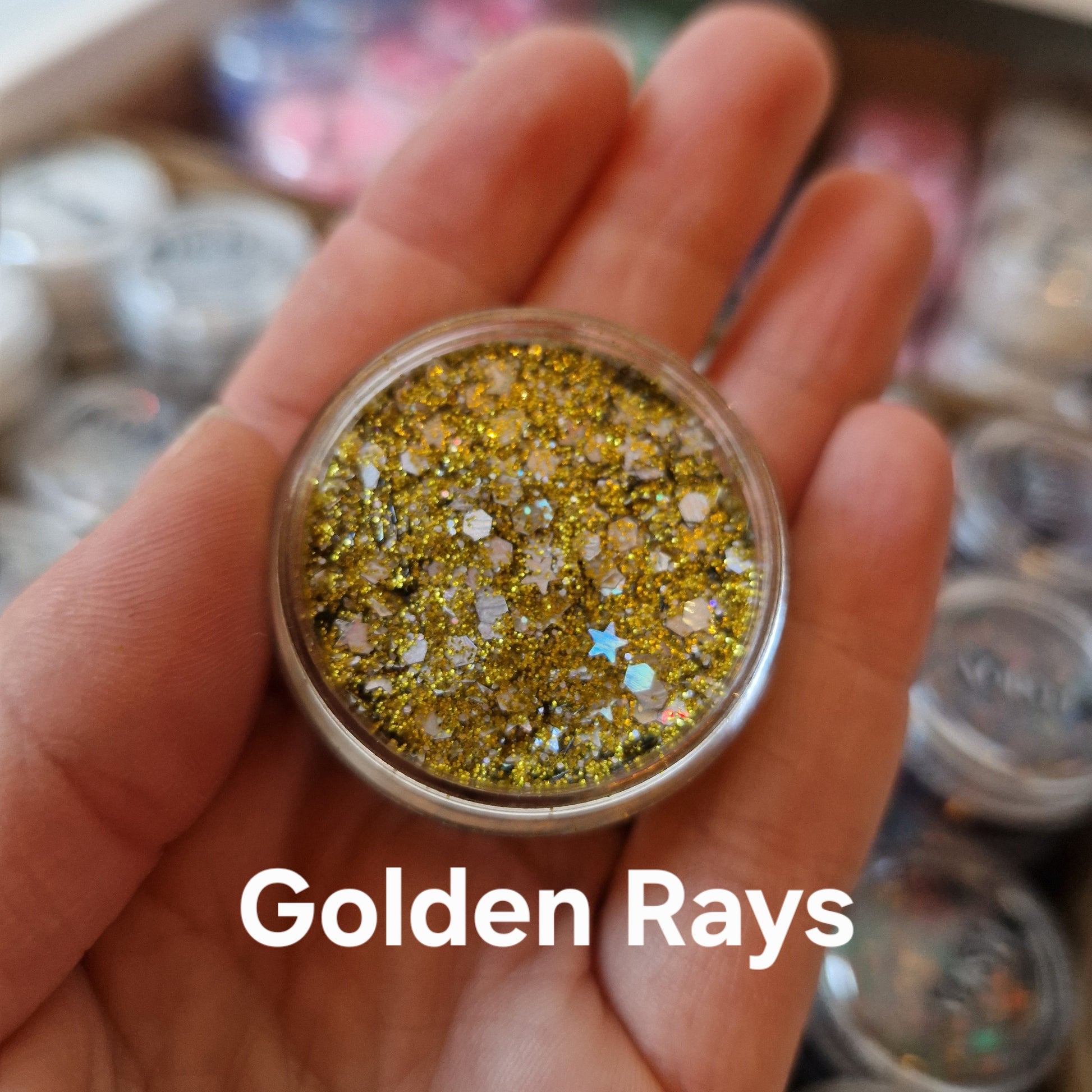 Golden Rays Glitter Cream - guldglitter med sparkle-effekt i åben beholder, holdt i hånd til makeup ogBodyArt design