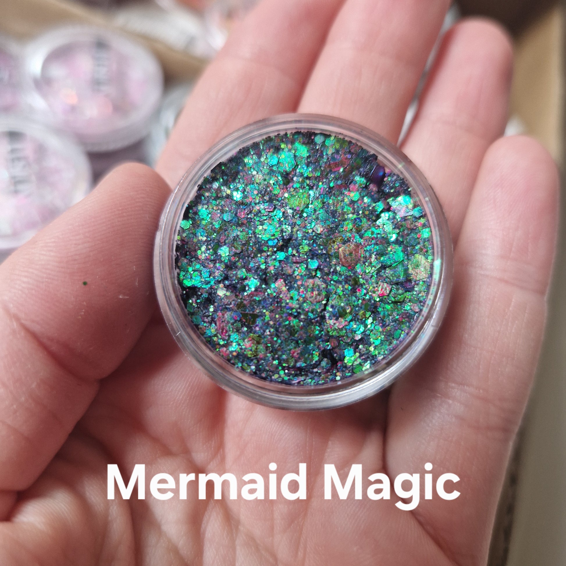 Mermaid Magic glitter cream i hånd viser iriserende grønne og turkise glitterpartikler på sort base til makeup og bodyart