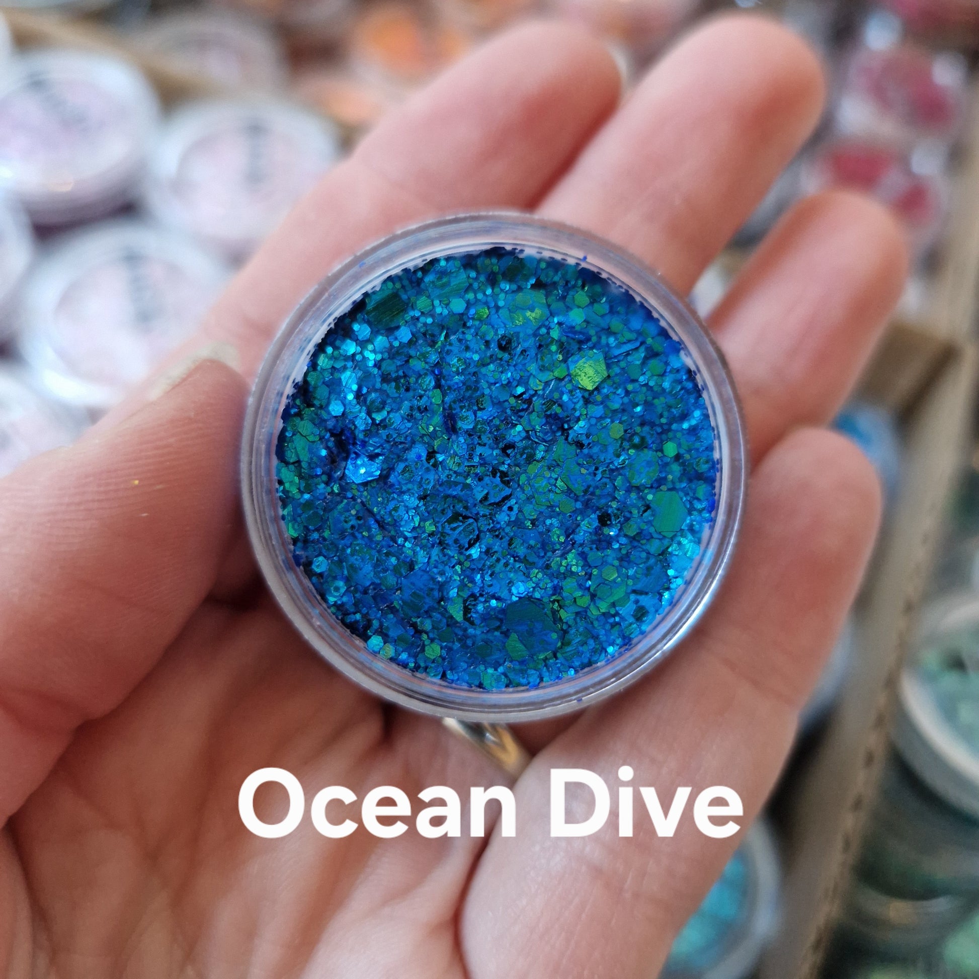 Ocean Dive Glitter Cream - blå og grøn glitter creme i transparent beholder holdt i hånd