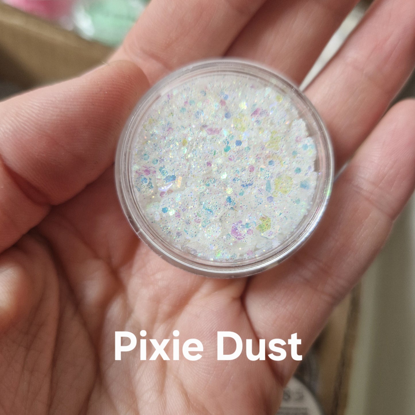 Pixie Dust glitter cream i hvid med farvede glitterpartikler holdt i hånd, viser produktets sparkly tekstur
