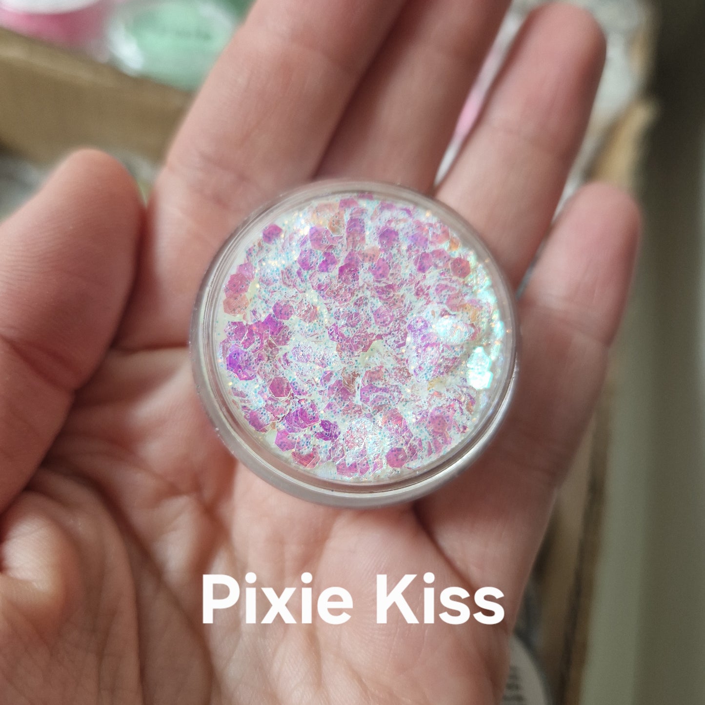 Pixie Kiss Glitter Cream i pink og lilla med shimmer-effekt, holdt i hånd for at vise produktets glitterkvalitet og farverige design.