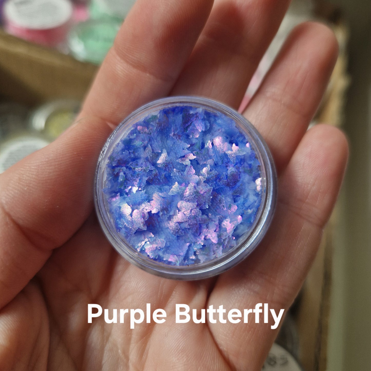 Purple Butterfly glitter cream viser intense blå og lilla glitter-flager i transparent cremebasis fra Fusion Body Art, holdt i hånd