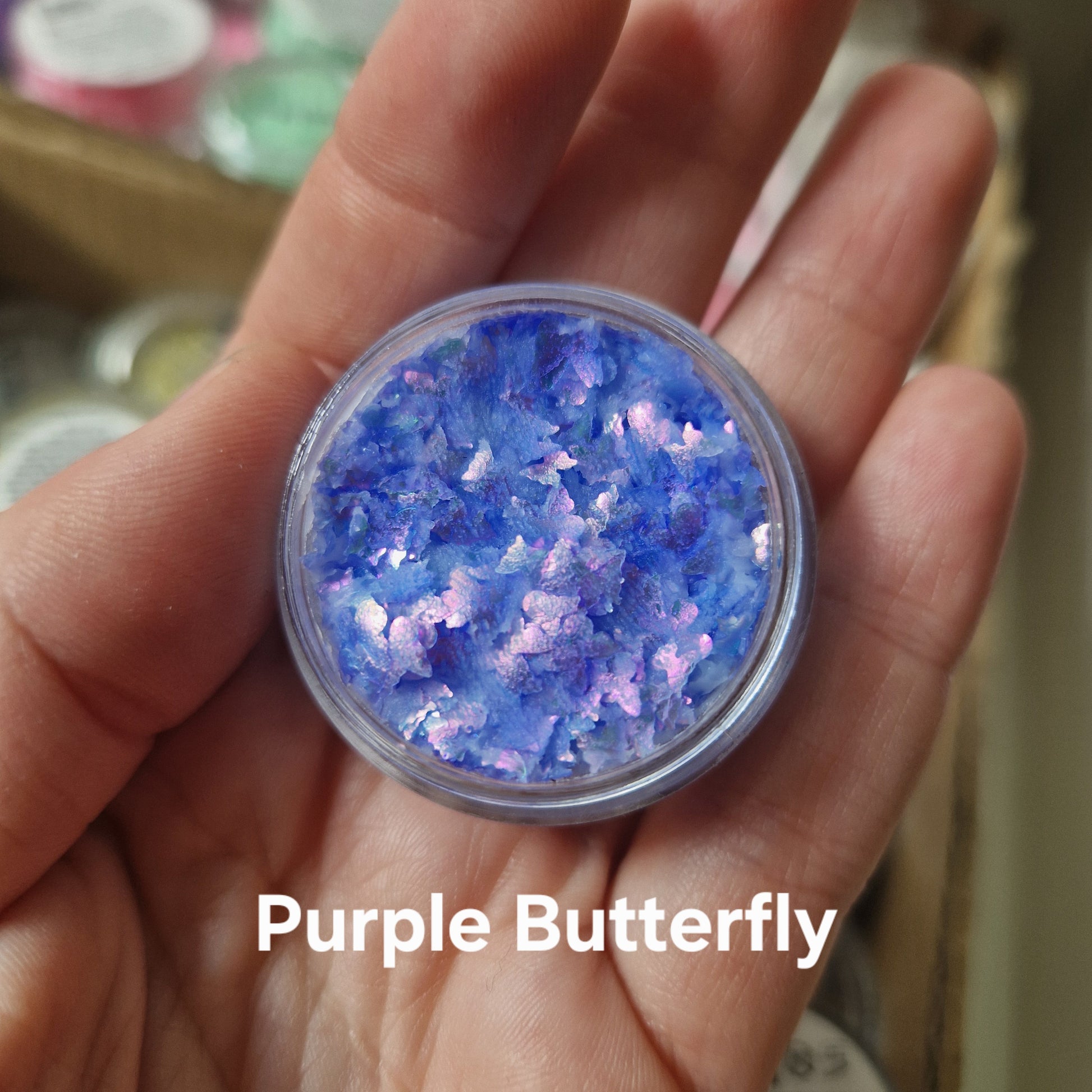 Purple Butterfly glitter cream viser intense blå og lilla glitter-flager i transparent cremebasis fra Fusion Body Art, holdt i hånd